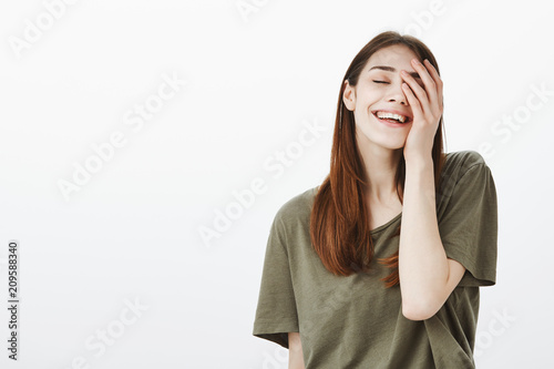 Portrait of pleased confident good-looking urban female in dark-green t-shirt, holding palm on face and smiling broadly, closing eyes, being happy and relaxed, feeling relieved after trip