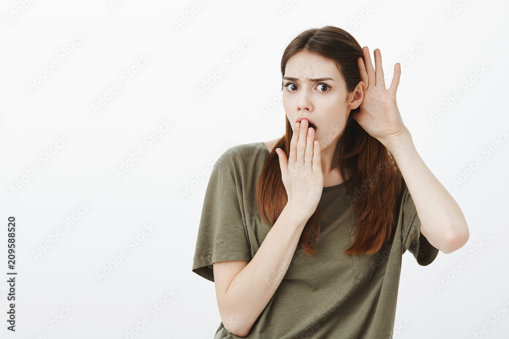 For God sake, who told you that. Portrait of shocked displeased attractive female student in casual clothes, holding hand near ear and opened mouth, frowning while overhearing awful gossip