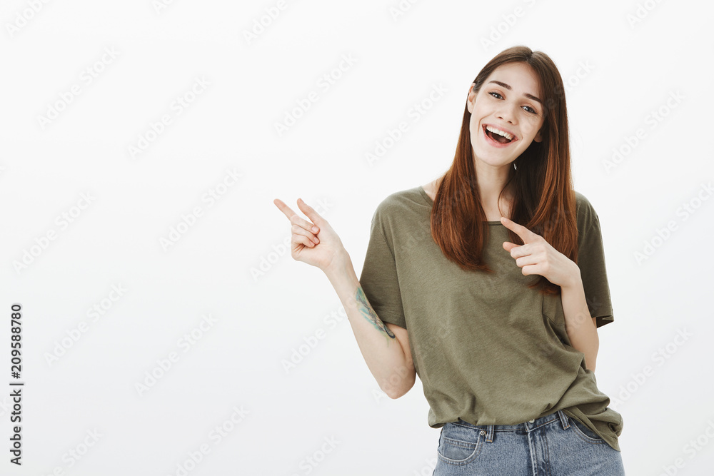 Studio shot of happy playful party woman with brown hair, smiling broadly and happily while pointing with index finger at upper left corner, advising great place to hang out and drink beer Studio shot of happy playful party woman with brown hair, smiling broadly and happily while pointing with index finger at upper left corner, advising great place to hang out and drink beer