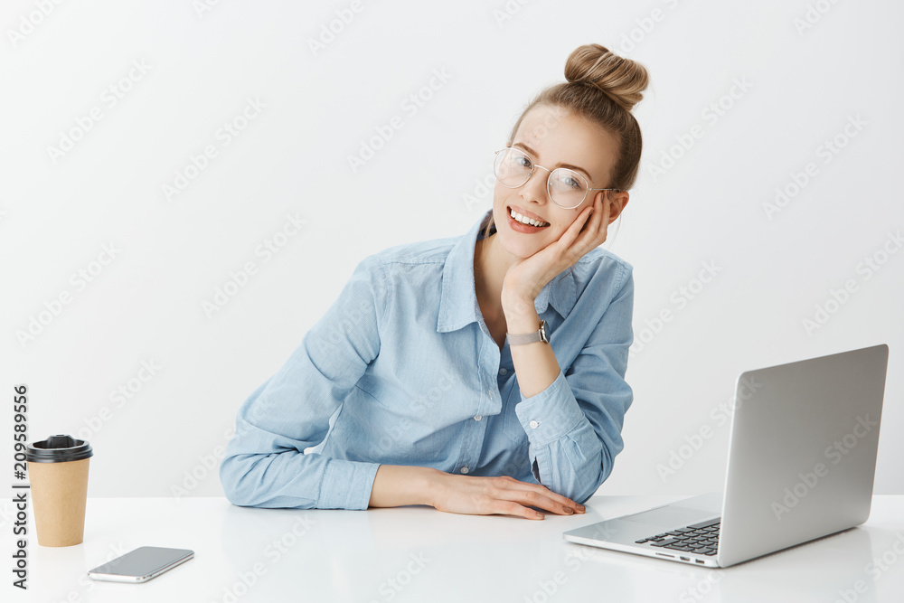 Girl sharing thoughts with coworker while sitting in office. Happy attractive woman in stylish outfit and glasses, leaning head on hand while sitting near smartphone and laptop, drinking cup of tea Girl sharing thoughts with coworker while sitting in office. Happy attractive woman in stylish outfit and glasses, leaning head on hand while sitting near smartphone and laptop, drinking cup of tea