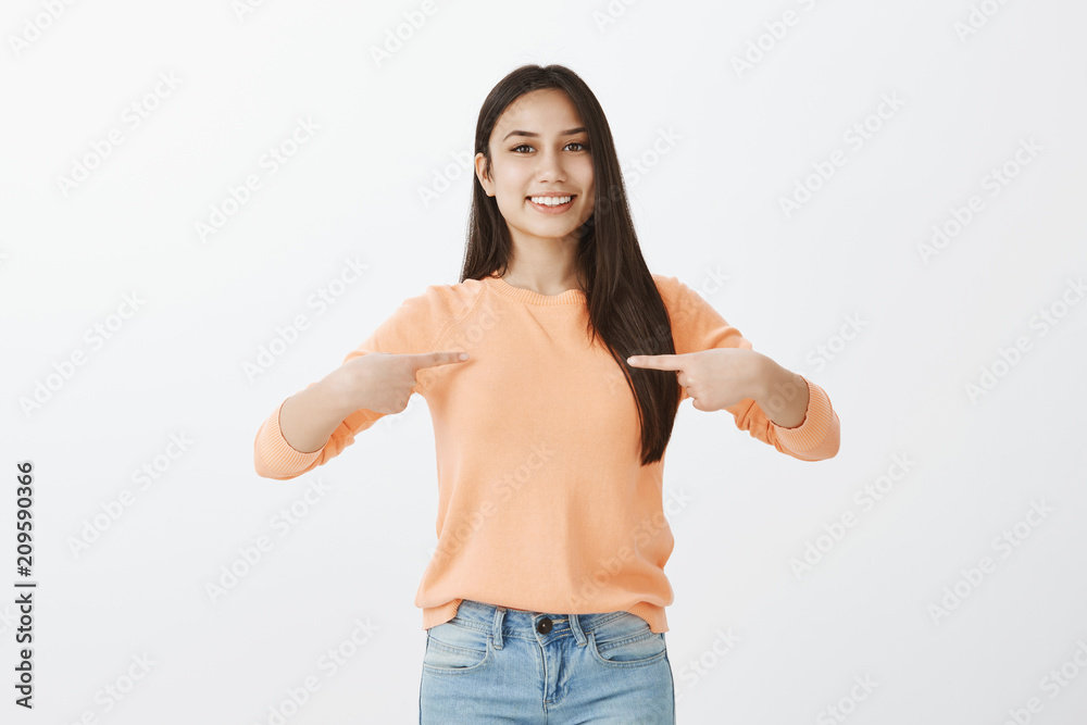 Portrait of proud good-looking adult female with long dark hair, wearing casual clothes and smiling broadly while pointing with both index fingers at chest, being happy and satisfied with good result Portrait of proud good-looking adult female with long dark hair, wearing casual clothes and smiling broadly while pointing with both index fingers at chest, being happy and satisfied with good result