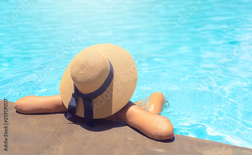 Woman with brown hat relaxing in swimming pool with blue water during a sunny day , holiday concept
