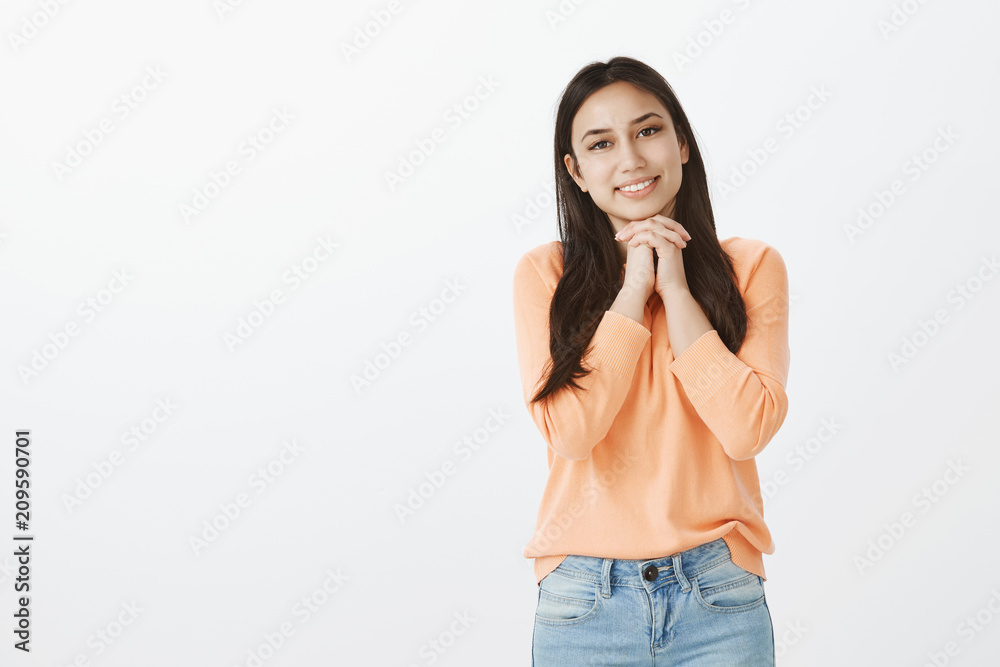 Studio shot of caring attractive woman in love in casual outfit, holding hands together above chest and smiling while gazing at camera with passion and romantic attitude, admiring pop star Studio shot of caring attractive woman in love in casual outfit, holding hands together above chest and smiling while gazing at camera with passion and romantic attitude, admiring pop star