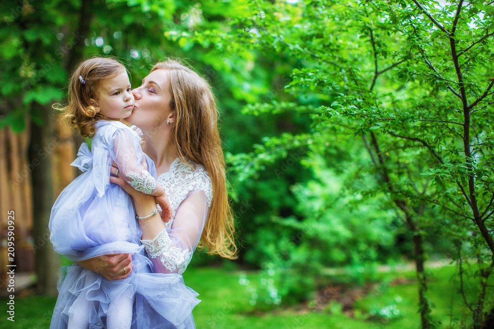 Beautiful mother in blue dress holds dear daughter and kisses her on cheek Beautiful mother in blue dress holds dear daughter and kisses her on cheek