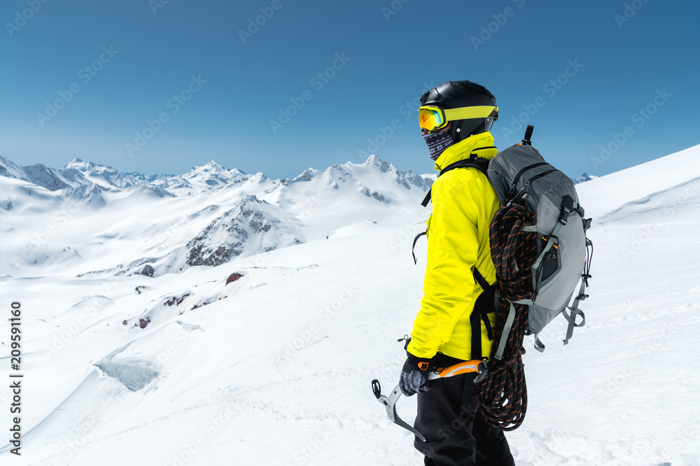 A mountaineer man holds an ice ax high in the mountains covered with snow. View from the back. outdoor extreme outdoor climbing sports using mountaineering equipment