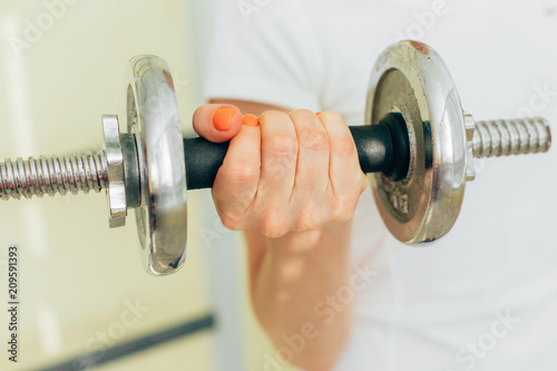 Young pretty woman in white shirt training with dumbbells at home. Fit girl doing exercise on biceps. Healthy lifestyle concept.