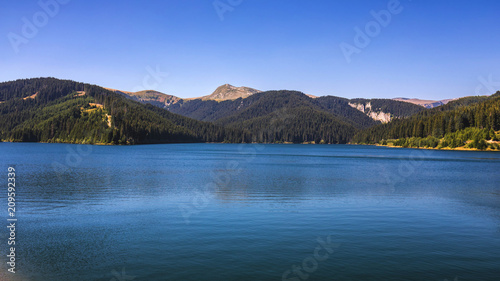 View to Bolboci lake from the damb with carpathian mountains at the background, Sinaia, Romania.