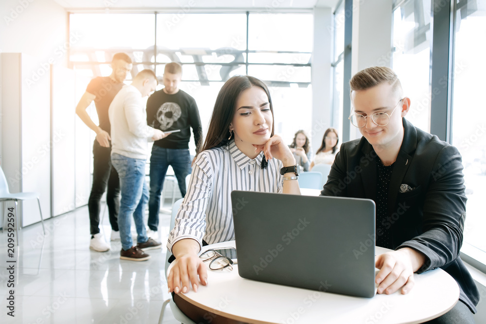 Beautiful young business couple are using a laptop, talking and smiling while working in office Beautiful young business couple are using a laptop, talking and smiling while working in office
