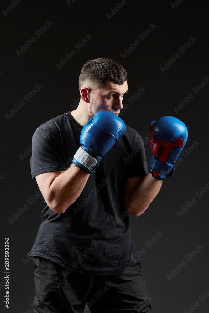 Low key studio portrait of handsome muscular fighter preparing for boxing on dark blurred background