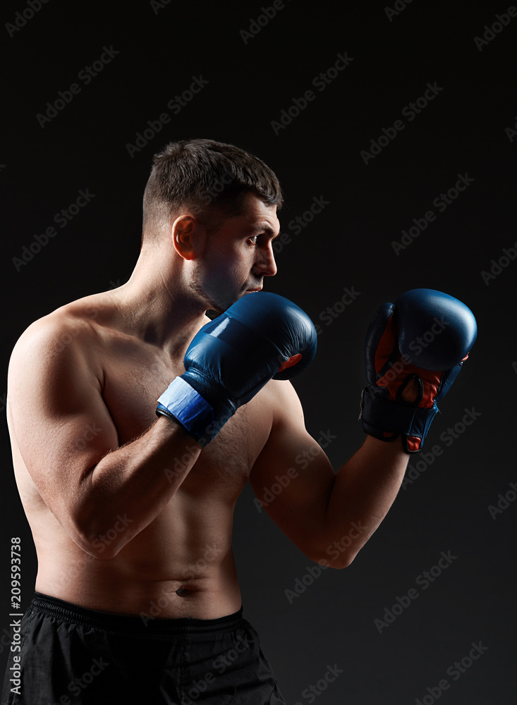 Low key studio portrait of handsome muscular fighter practicing boxing on dark blurred background