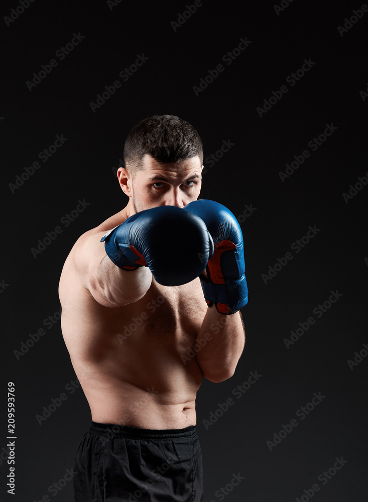 Low key studio portrait of handsome muscular fighter practicing boxing on dark blurred background