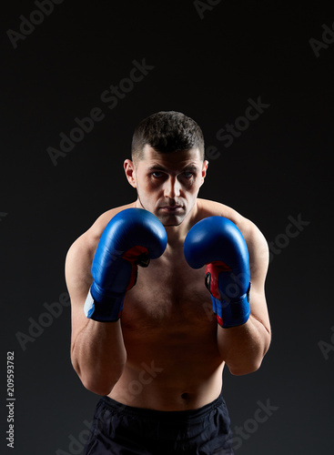 Low key studio portrait of handsome muscular fighter practicing boxing on dark blurred background © Aleksey