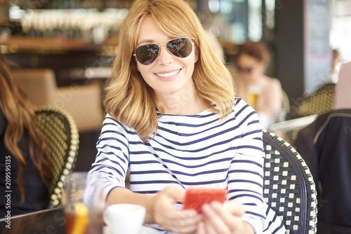 Beautiful middle aged woman with coffee and mobile phone at outdoor cafe