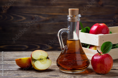 Apple cider vinegar and fresh red apple on a wooden background photo