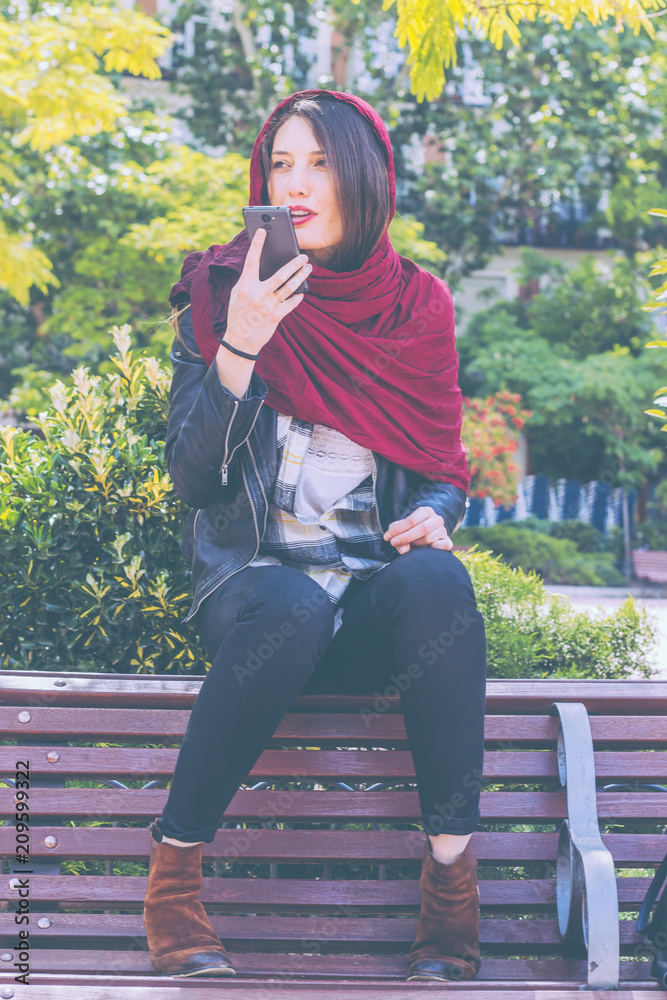 Woman using smartphone voice recognition outdoors in the city park. Woman using smartphone voice recognition outdoors in the city park.