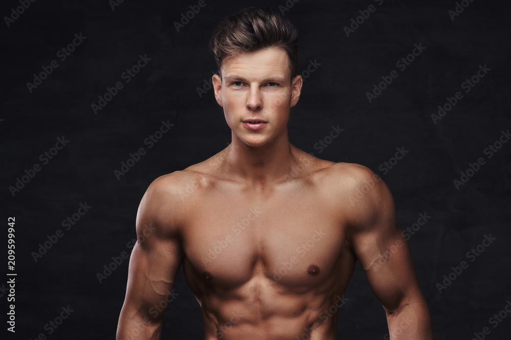 Close-up portrait of a sexy shirtless young man model with a muscular body and stylish haircut posing at a studio. Isolated on dark background.
