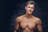 Close-up portrait of a sexy shirtless young man model with a muscular body and stylish haircut posing at a studio. Isolated on dark background.
