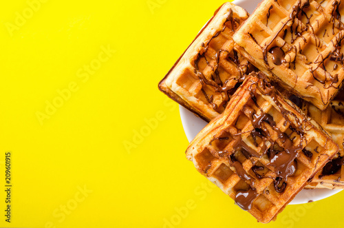 Belgian waffles on a plate of chopped chocolate on a yellow background. Sweets, dessert. Copy space photo
