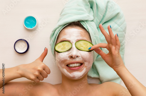 Woman laying on the beautician table in a salon with sour cream over her face and with cucumber slice on her eyes. Face skin care concept.