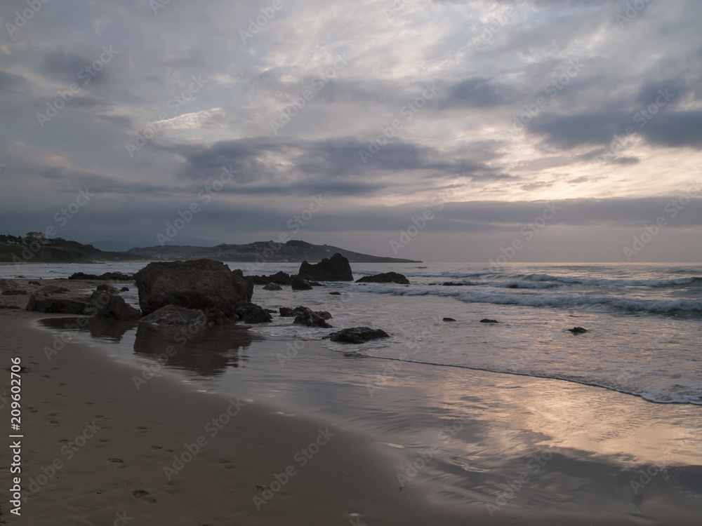 Puesta de sol entre nubes en la bonita playa de Liencres en Cantabria Puesta de sol entre nubes en la bonita playa de Liencres en Cantabria
