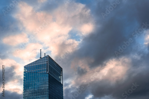Modern glass office building against dramatic blue and yellow sky.