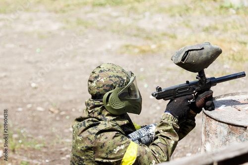 Paintball player in protective uniform and mask aiming gun in the forrest cover. A young man is preparing to shoot. The concept of active recreation, team play. Selective focus