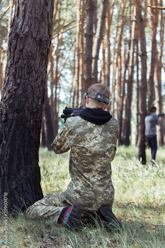 Young boy in camouflage with a gun, plays laser tag in the forest. Lasertag shooting game in open air. Military sport. Simulation of military operations