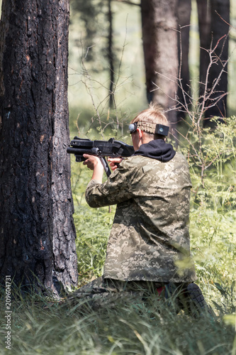 Young boy in camouflage with a gun, plays laser tag in the forest. the guy is aiming. Lasertag shooting game in open air. Military sport. Simulation of military operations