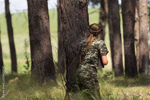 Girl in camouflage with a gun, plays laser tag in the forest. the player is aiming. Lasertag shooting game in open air. Military sport. Simulation of military operations