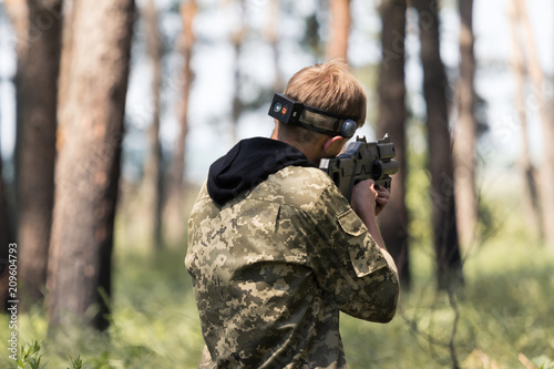 Young boy in camouflage with a gun, plays laser tag in the forest. the guy is aiming. Lasertag shooting game in open air. Military sport. Simulation of military operations