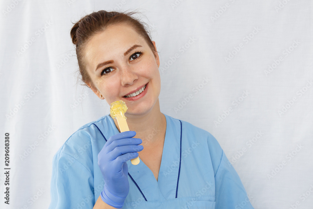 Smiling woman doctor beautician holds a spatula with sugar paste in her hand. Horizontal frame. Smiling woman doctor beautician holds a spatula with sugar paste in her hand. Horizontal frame.