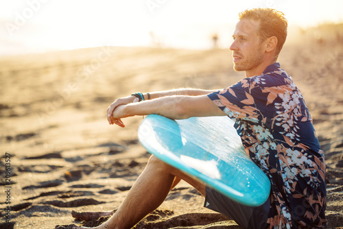 Photography Portrait of happy surfer in hawaiian t-shirt walking with surf board on the beac