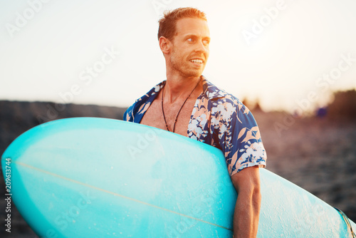 Canvas Print Portrait of happy surfer in hawaiian t-shirt walking with surf board on the beac