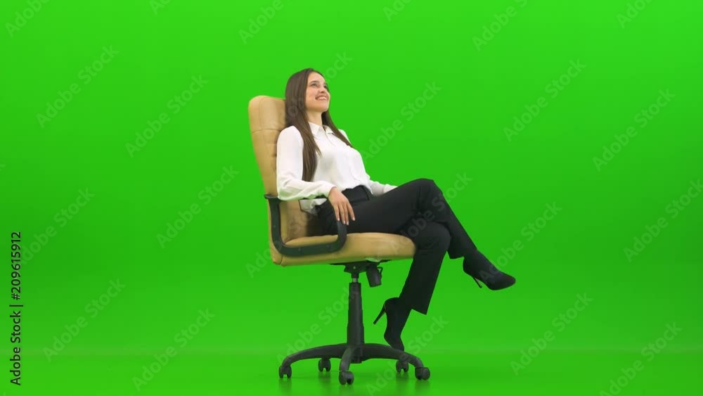 The businesswoman sitting on the office chair and laughing on a green background