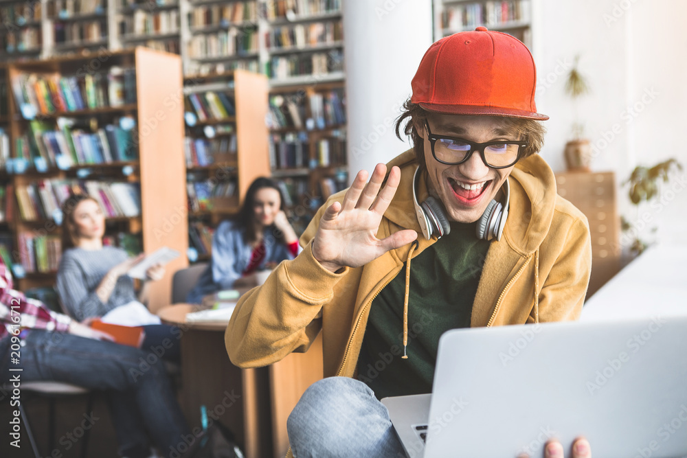 Portrait of outgoing male gesticulating hand while watching at laptop in library Portrait of outgoing male gesticulating hand while watching at laptop in library