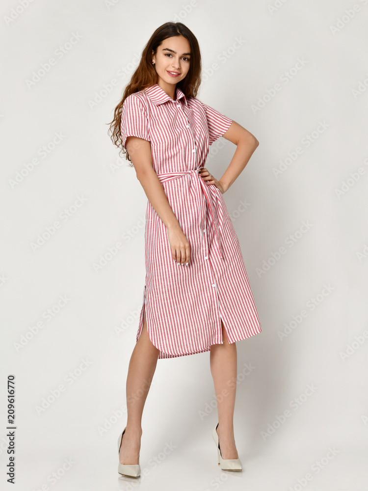 Young beautiful woman posing in new pink stripes casual summer dress on grey Young beautiful woman posing in new pink stripes casual summer dress on grey