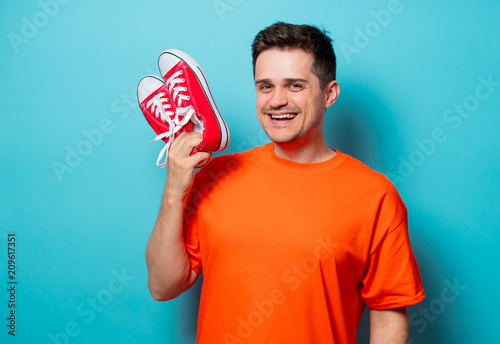 Young handsome man in orange t-shirt with red gumshoes. Studio image on blue background © Masson
