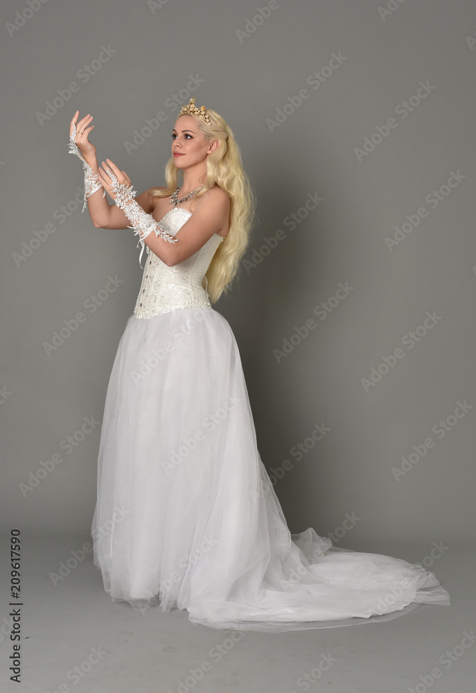 Naklejka premium full length portrait of blonde girl wearing white fantasy gown. standing pose in side profile, grey studio background.