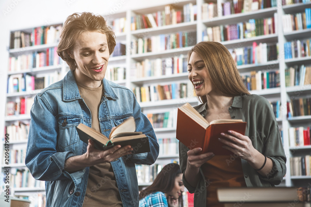 Portrait of positive man talking with satisfied lady while locating in library. They holding volumes in hands. Positive study concept