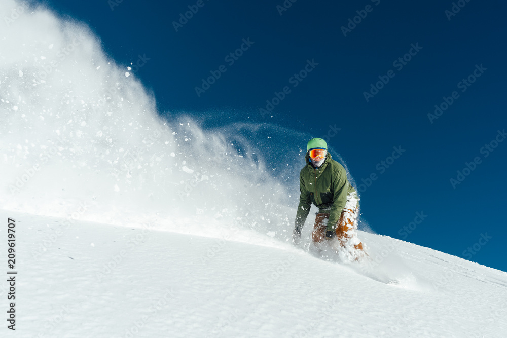 male snowboarder curved and brakes spraying loose deep snow on freeride  slope