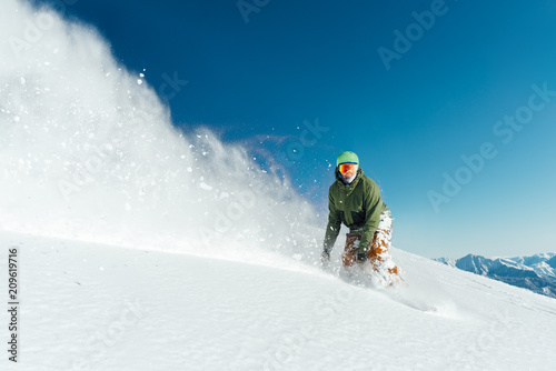 male snowboarder curved and brakes spraying loose deep snow on freeride slope