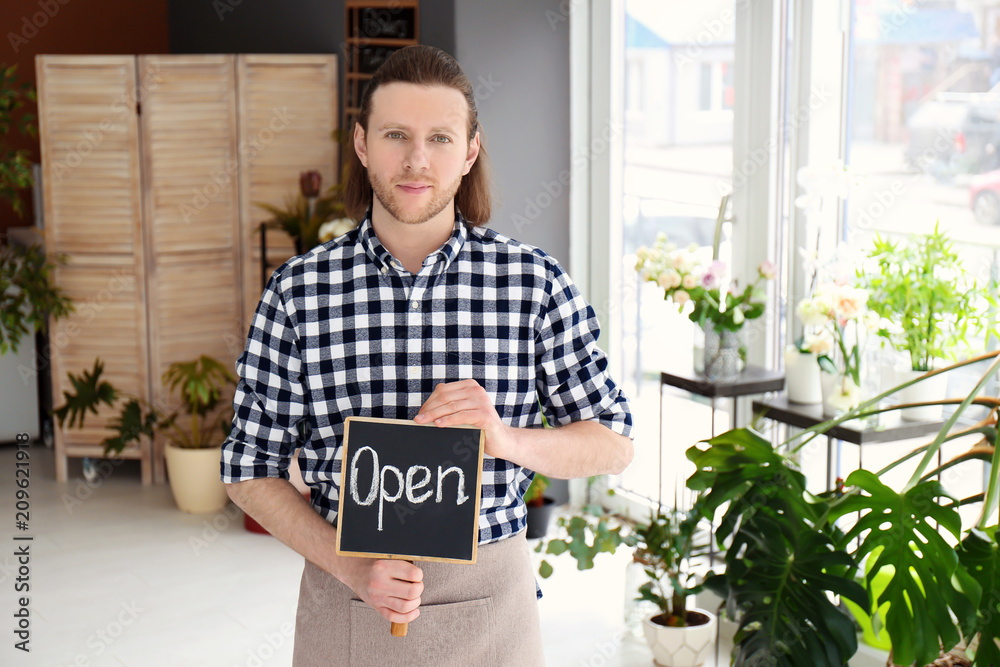 Fototapeta premium Male florist holding OPEN sign at workplace