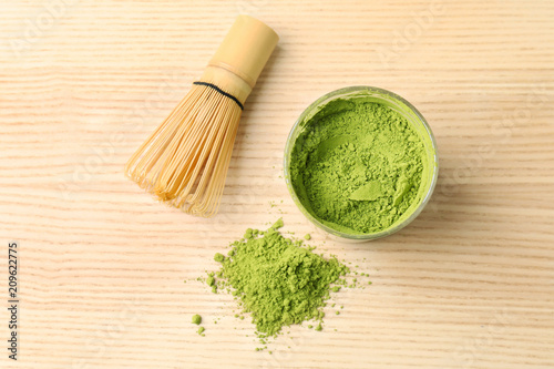 Powdered matcha tea and chasen on wooden background, top view