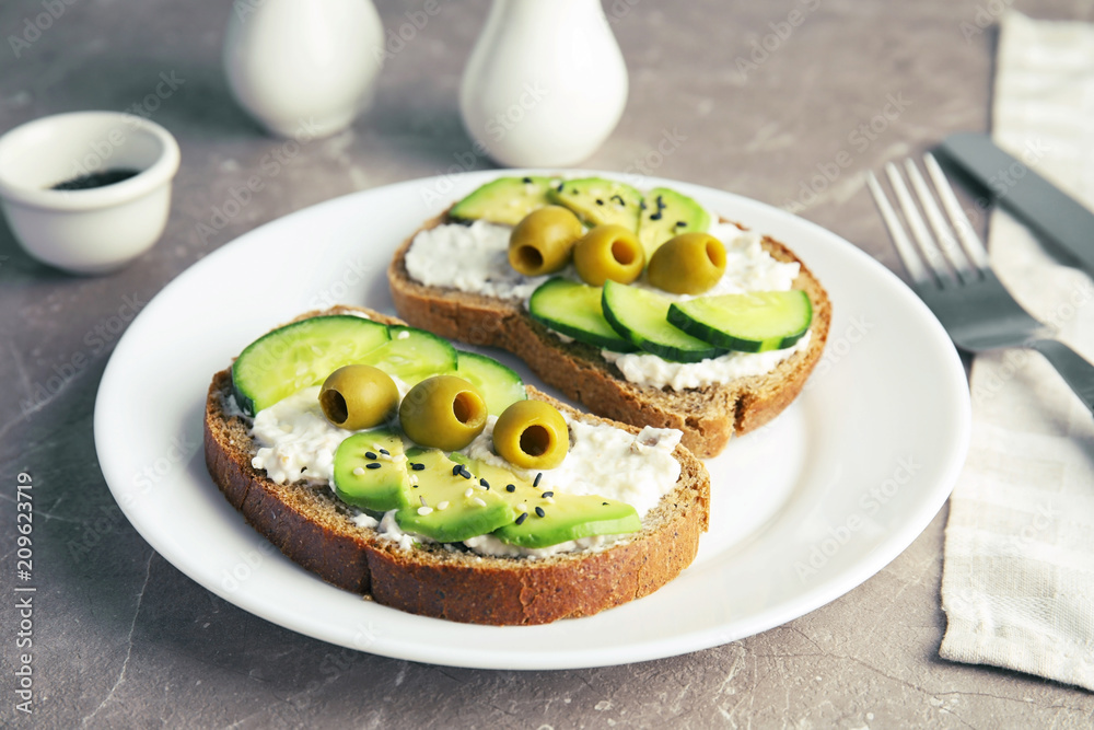 Crisp rye toasts with sliced avocado, cream cheese and olives on plate, closeup