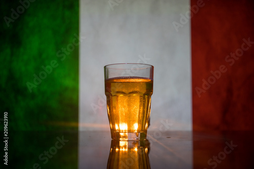 Creative concept. Pint of fresh beer on grass with blurred flag of Italy on background or Glass of lager beer ready for drink. Copy space.
