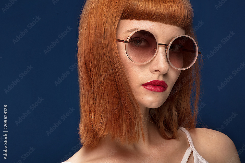 Beautiful redhead girl in sunglasses on blue background. Beautiful redhead girl in sunglasses on blue background.