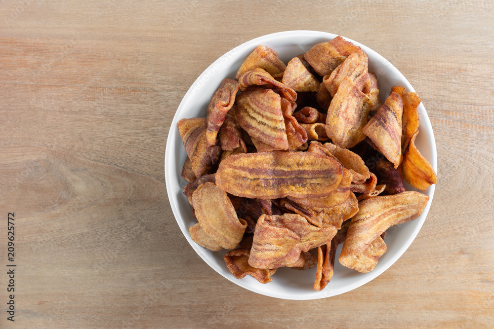 top view of deep fried banana chips in a ceramic bowl on wooden table, asian style delicious snack. top view of deep fried banana chips in a ceramic bowl on wooden table, asian style delicious snack.