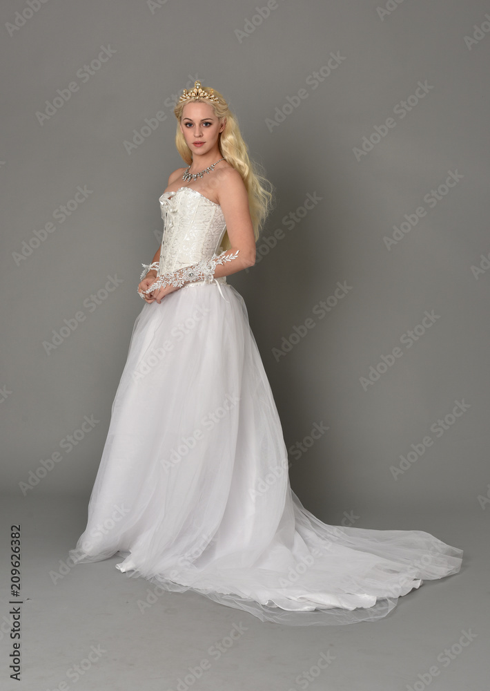 Fototapeta premium full length portrait of blonde girl wearing white fantasy gown. standing pose in side profile, grey studio background.