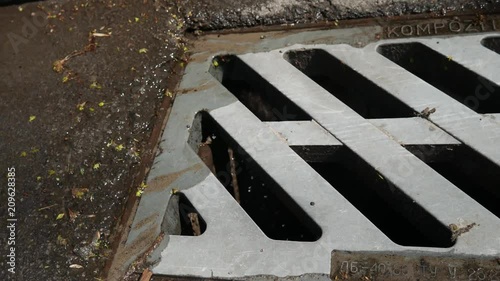 Rain water flowing into a drain.Rainwater flows on the asphalt road and fall into the metal hatch with holes drain.Rainwater flows on the road and fall into the metal hatch with holes drain.