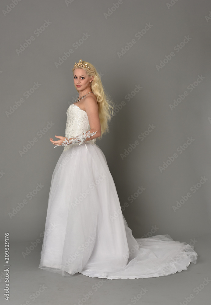 full length portrait of blonde girl wearing white fantasy gown. standing pose in side profile, grey studio background. full length portrait of blonde girl wearing white fantasy gown. standing pose in side profile, grey studio background.